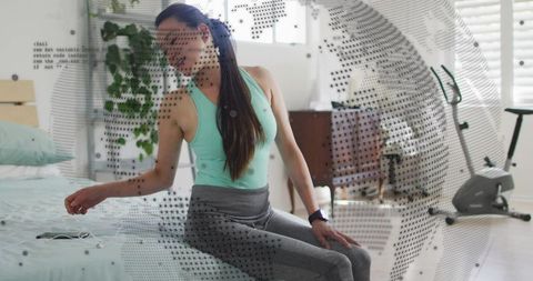 Korean woman sitting on bed reaching for phone with digital globe overlay for fitness wellness