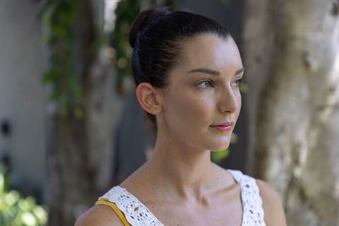 Serene middle-aged woman gazing right in garden wearing white crochet top and yellow strap
