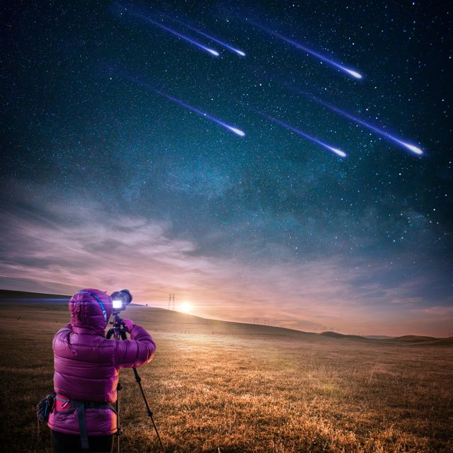 Photographer under starry night sky capturing a breathtaking meteor shower on tripod. This image can be used for astronomy magazines, educational materials, travel brochures, inspiring photography blogs, and more.