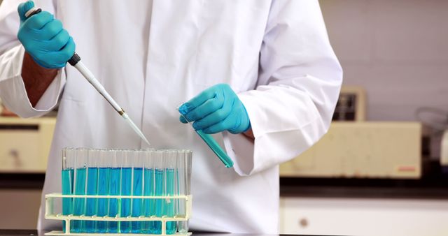 A scientist in a lab coat and gloves is pipetting a blue liquid into a test tube rack, with copy space. Their precise technique reflects the meticulous nature of scientific research and experimentation.