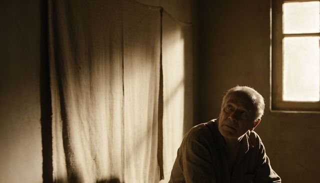 Senior man sitting and gazing toward window in sunlit moody interior