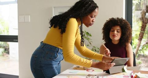 Diverse women collaborating over tablet and color swatches, reviewing design palette