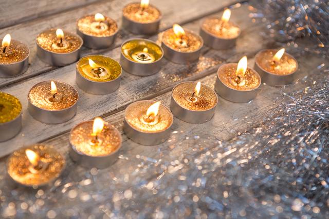 Tealight candles with golden glitter burning on a wooden plank, creating a warm and cozy ambiance. Suitable for holiday and festive decoration themes, Christmas celebrations, and winter season promotions.