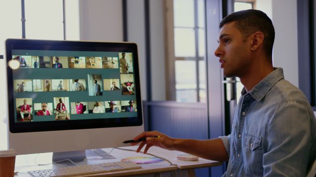 Young graphic designer intently selecting images on a computer in a sleek, modern office space. This scene captures the professional environment and creative processes involved in graphic design. Ideal for use in articles or materials relating to creative professions, digital work environments, or the design industry. Highlights innovative workspace and technical skills.