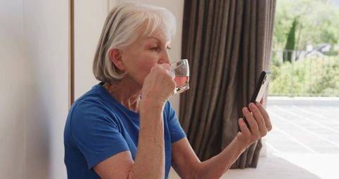 Senior Woman Enjoying Beverage while Using Smartphone