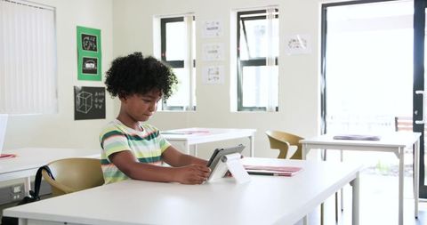 Curious African American Boy Using Tablet in Bright Classroom for Digital Learning