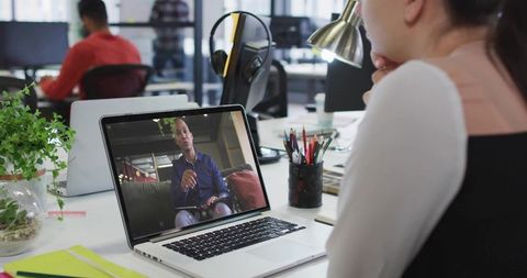 Young woman attending remote video meeting on laptop in bright open office coworking