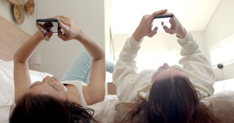 Teen Friends Relaxing on Bed Using Smartphones