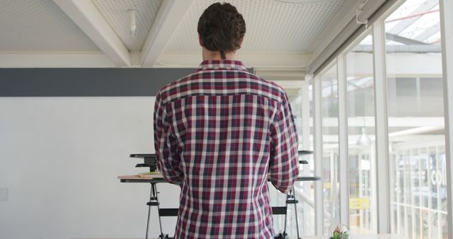 Man standing at standing desk in a modern office. Perfect for illustrating concepts of ergonomics, productivity, modern workspaces, and casual office environments.