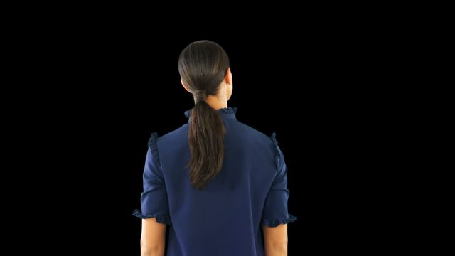 A woman with long hair pulled back in a ponytail, wearing a blue blouse, stands against a dark backdrop. Useful in corporate presentations, leadership seminars, blogs on women's empowerment, or articles discussing career contemplation and ambitions.