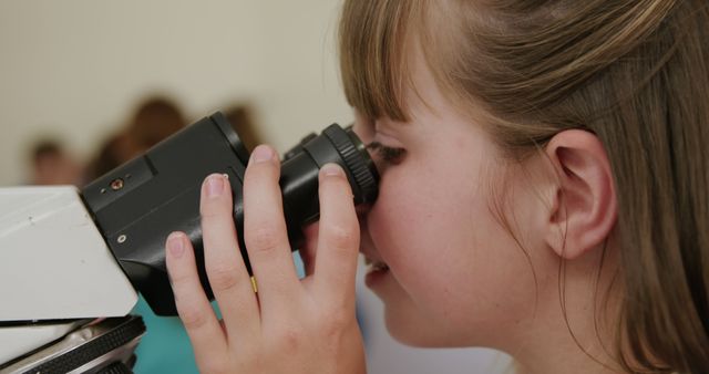 Happy caucasian schoolgirl using microscope in elementary school science class. Science, childhood, education, learning and elementary school, unaltered.