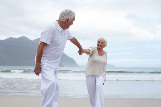Senior couple enjoying a walk on the beach, holding hands and smiling. Perfect for promoting retirement lifestyle, travel destinations, senior health and wellness, and romantic getaways for older adults.