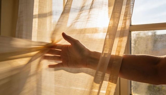 Reaching hand touching sheer curtain in golden morning sunlight casting soft warm glow