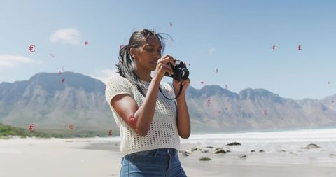 Woman photographing coastal landscape with dslr on sandy beach near mountains