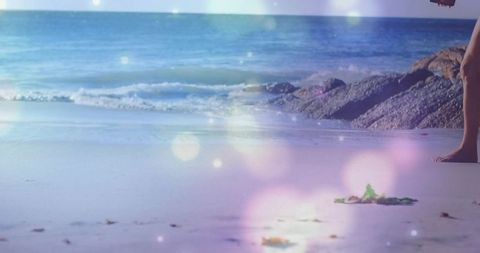 Walking barefoot along sunlit beach shoreline with gentle waves and dreamy lens flare