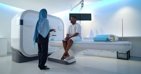 African american clinician wearing hijab consulting male patient on mri scanner table