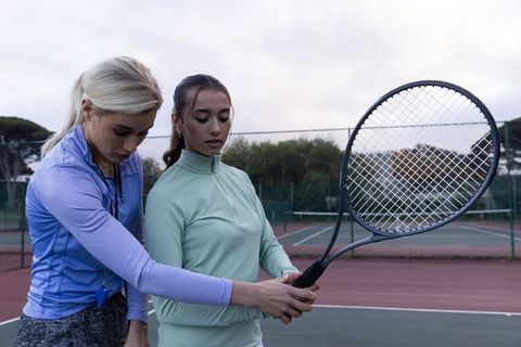 Tennis coach adjusting student grip during lesson on outdoor hard court at dusk