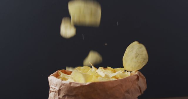 Close up view of potato chips falling in a paper bag against black background - Download Free Stock Photos Pikwizard.com