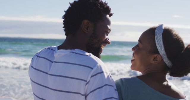 African american couple smiling, embracing and talking on the beach. healthy outdoor leisure time by the sea.
