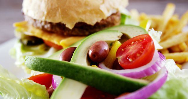 A close-up view of a fresh salad with ripe tomatoes, crisp lettuce, and olives, accompanied by a juicy burger and fries in the background. Vibrant colors and textures invite a sensory experience of a classic American meal.