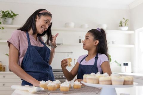 African american mother and daughter decorating cupcakes together in bright modern kitchen