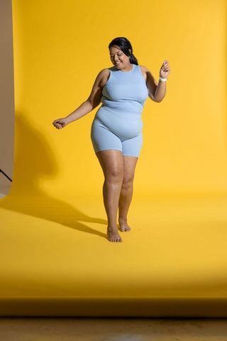 Confident african american woman dancing in light blue activewear on yellow backdrop