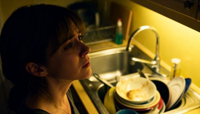 Overwhelmed woman pausing at sink with piled dishes under warm kitchen light