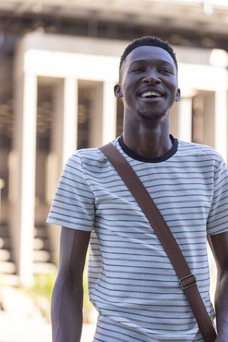 African american man standing smiling wearing striped tee and crossbody bag by colonnade
