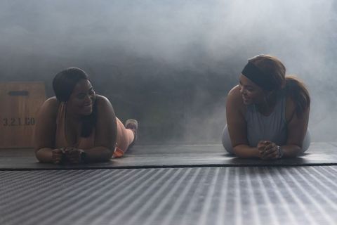 Plus-size african american women doing forearm plank together in dim smoky gym lighting