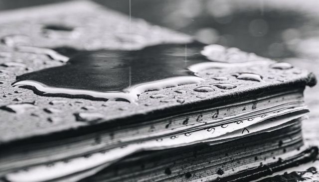 Weathered journal soaking in rain with ink-stained pages and water droplets