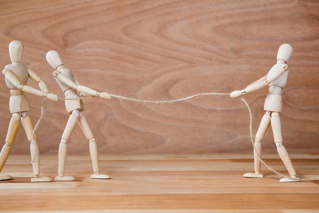 Wooden figurines are engaged in a tug-of-war game on a wooden surface. This image can be used to represent concepts such as teamwork, competition, conflict, and collaboration. Ideal for business presentations, team-building materials, and motivational content.