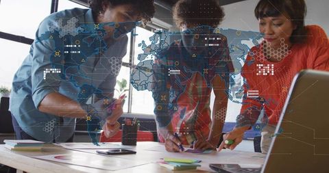 Collaborating team leaning over table with global data overlay and analytics visualization
