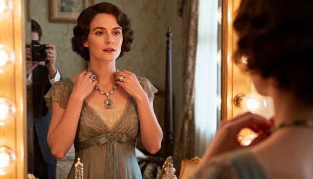 Adjusting vintage gown and fastening ornate pendant at lit vanity mirror, boudoir glamour