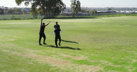 Recreational cricketers celebrating wicket on sunny suburban sports field in casual match