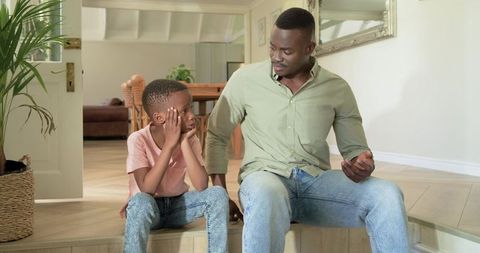 African american father sitting and talking with son on home steps, gentle conversation
