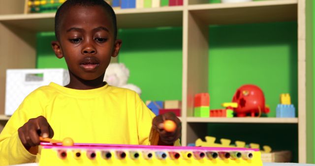 Young boy in yellow shirt playing a xylophone amid a vibrant and educational play space with toys. Ideal for content on childhood learning, musical education, vibrant play spaces, early childhood development, and joyful playtime activities.