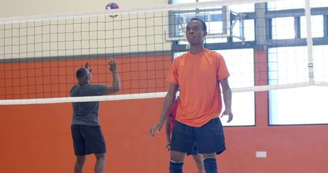 African american male volleyball team blocking at indoor gym match wearing knee pads