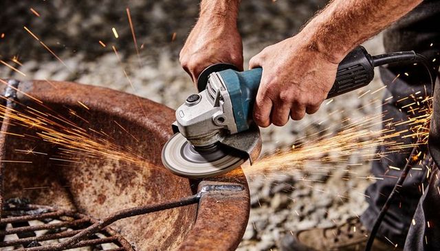 Hands holding angle grinder grinding rusty metal bowl, flying sparks, outdoor metalwork