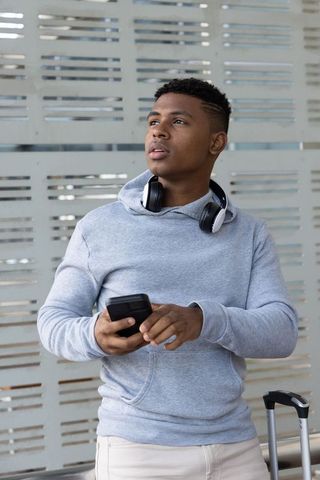 African american traveler standing with smartphone and headphones at airport terminal