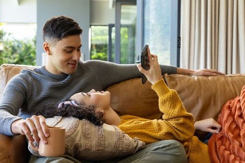 Young couple relaxing on leather couch, woman scrolling smartphone, cozy home moment