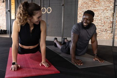 Smiling workout partners doing upward stretch on red and gray mats in industrial gym