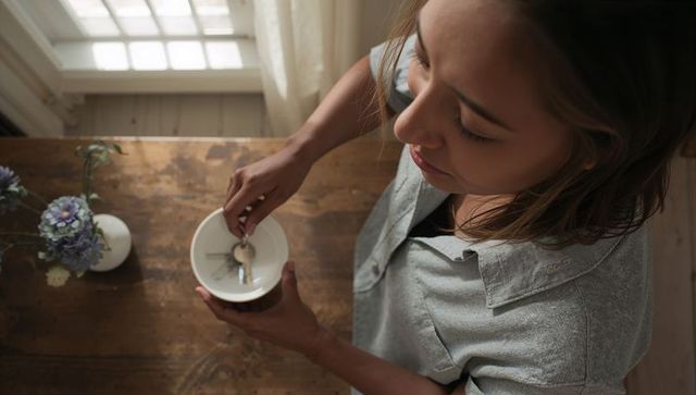 Asian woman placing keys into ceramic bowl on wooden table by sunlit window with flowers