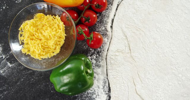 This image features a set of pizza ingredients being prepared, with a rolled out dough, shredded cheese in a bowl, red and yellow bell peppers, and cherry tomatoes on the vine. Ideal for websites and blogs focusing on recipes, home cooking, and culinary arts. Use it to illustrate cooking tutorials, food preparation guides, or promotional material for restaurants and pizzerias.