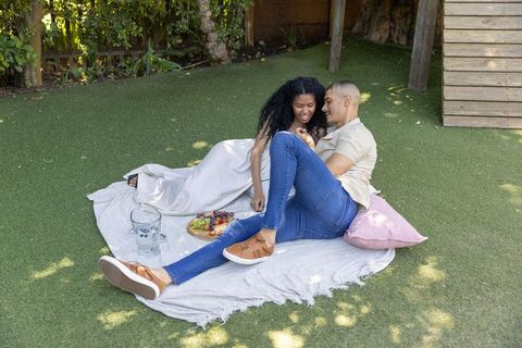 Couple enjoying romantic backyard picnic reclining on blanket sharing fruit platter