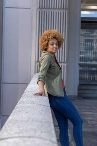 African american woman leaning on concrete railing on urban terrace, fashion portrait