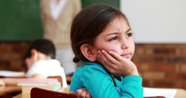 Young girl sitting at a school desk, appearing deep in thought and daydreaming. Great for educational content, school themes, elementary learning materials, and childhood behavior studies.
