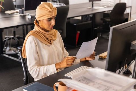 Focused businesswoman in hijab analyzing documents at modern workspace