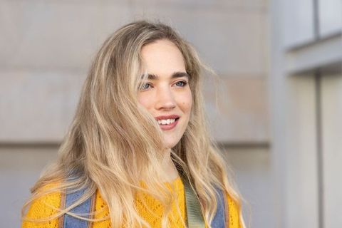 Smiling young woman wearing yellow sweater and backpack against modern urban stone facade
