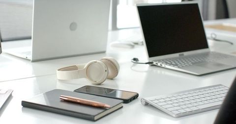 Minimal modern office workspace featuring white headphones, laptop, smartphone, notebook