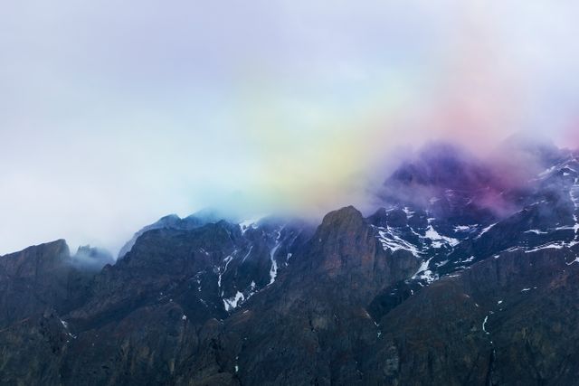 Vibrant rainbow appears over misty and rugged mountain peaks, creating a serene and captivating visual. Suitable for use in travel brochures, nature magazines, or as inspirational art in home and office decor.